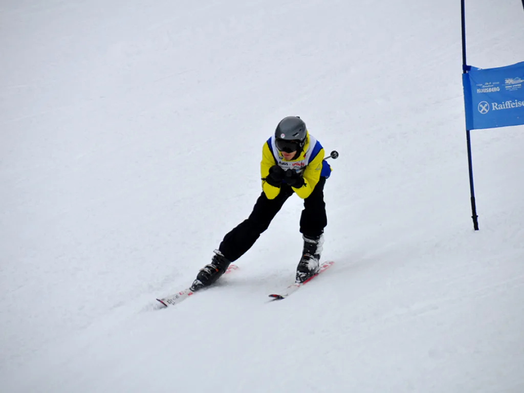 Skifahrer in gelber Hose in der Kurve am blauen Tor.